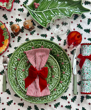 Christmas-themed table setting with green plates, red bows, and a patterned tablecloth.