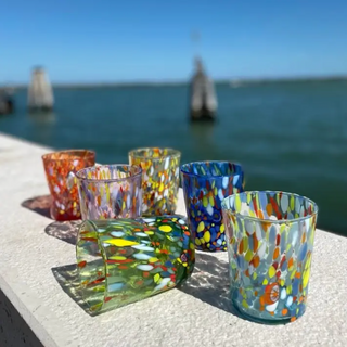 Colorful glass tumblers on a ledge with a blurred water and sailboat background
