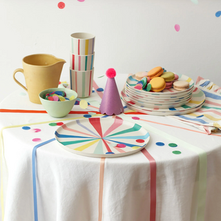 Colorful table setting with plates, cups, and macarons on a white tablecloth.