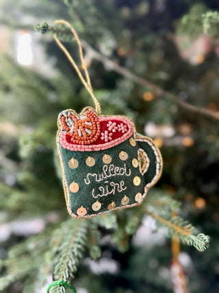 Decorative ornament shaped like a mug with polka dots and text, hanging on a Christmas tree.