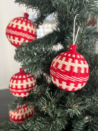 red and natural iraca palm christmas baubles hanging on a tre