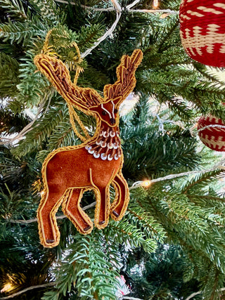 Decorative reindeer ornament on a Christmas tree with lights and other ornaments.